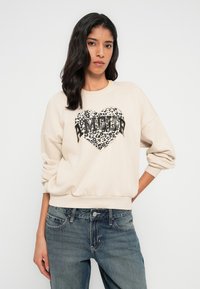 Μπεζ φουτεράκι με καρδιά σε σχέδιο λεοπάρ και το κείμενο "AMOUR" μαύρο. Διαθέτει άνετη εφαρμογή και ριμπ μανσέτες. Συνδυάζεται με μπλε τζιν.