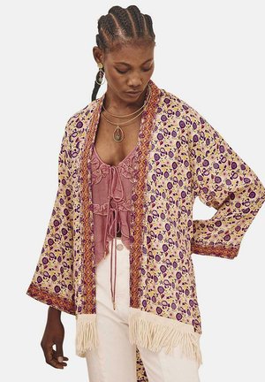 Cardigan de estilo kimono con un patrón floral y geométrico en púrpura, amarillo y naranja. Presenta flecos en el dobladillo y mangas anchas.