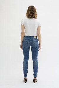 Pustite modre denim hlače s srednje visokim pasom, zadnjimi žepi in rumenim etiketom blagovne znamke. V kombinaciji z enostavno belo majico.