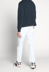 Marineblauw sweatshirt, witte slim-fit broek en kleurrijke sneakers. Beschikt over lange mouwen, geribbelde boorden en een logo-opdruk op de achterkant.