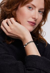 Czarny bransoletka z trzema koralikami, dwoma białymi i jednym ciemnym, na wielokolorowych sznurkach. Tekstura jest gładka z warstwowym wzorem.