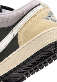 Κοντινό πλάνο της φτέρνας ενός πολύχρωμου αθλητικού παπουτσιού με μπεζ σουέντ, μαύρη σόλα, λευκά ράμματα και ανάγλυφο λογότυπο στην πάνω πλευρά.