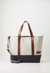 Sac en toile avec des poignées en cuir marron et un fond bleu marine. Il dispose d'une bandoulière réglable et d'une étiquette de marque sur le côté.