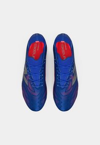 Μπλε αθλητικά παπούτσια με υφή στην επάνω πλευρά, με μια γκράντιεντ απόχρωση που μεταβαίνει σε ροζ. Περιλαμβάνουν ενωμένες λωρίδες και λεπτομέρειες με το λογότυπο.