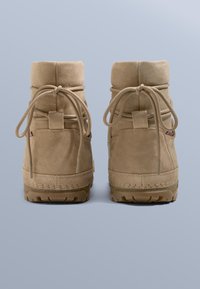 Beigefärgade ankelboots i mocka med rundade ovansidor, knutna snören och en greppvänlig sula. Har en liten logotyp nära hälen och en vadderad insida.