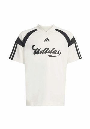 Dos adolescentes sonrientes que llevan camisetas deportivas blancas de Adidas con detalles en negro y pantalones cortos negros a juego con rayas blancas.