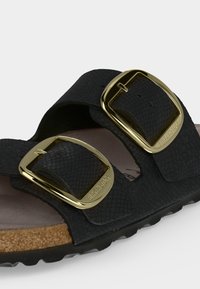 Μαύρο σανδάλι Birkenstock με υφή, δύο φαρδιές λουριά με μεγάλες χρυσές αγκράφες και πάτο από φελλό.