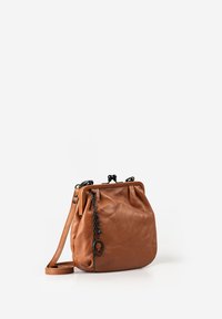 Bruine leren crossbodytas met zwart metalen sluiting en decoratieve zwarte kettinghanger, afgebeeld tegen een witte achtergrond.