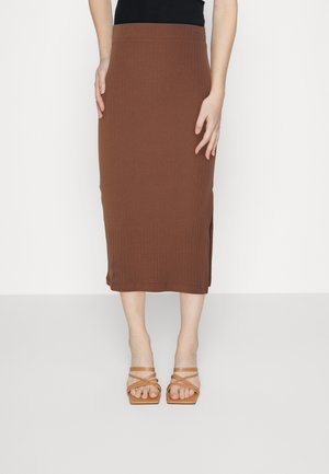 Brun ribbet midi-nederdel båret med tanfarvede sandaler med firkantet tå og stropper på en stående person mod en ensfarvet baggrund.