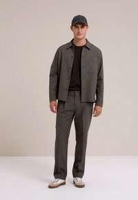 Szara kurtka w kratę z brązowymi guzikami na czarnej koszuli, zestawiona z pasującymi spodniami w kratę i białymi trampkami z brązowymi akcentami.