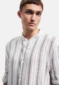 Witte gestreepte shirt met een bandkraag, knoopsluiting en textuur met dunne zwarte en grijze lijnen, met een visgraatpatroon.