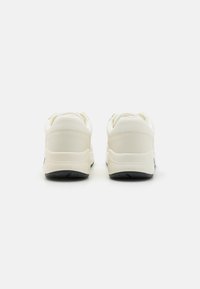 Baskets blanches avec une tige en synthétique lisse, un col rembourré et une semelle en caoutchouc noir texturé avec des motifs de traction.