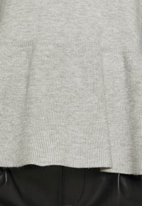 Miękki szary sweter o prążkowanym wykończeniu z delikatnym marszczeniem nad czarnymi skórzanymi spodniami.