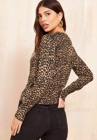 Halenka s leopardím potiskem, dlouhým rukávem a kulatým výstřihem, vyrobená z měkkého materiálu. Kombinována s černými kalhotami s vysokým pasem.
