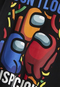 Sort T-shirt med farverigt grafisk tryk af tre farvede medspillere (rød, orange, blå) med legesyg konfetti og ordet "SUSPICIOUS."