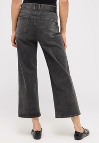 Bredde ben sorte denimjeans med høj talje, syninger, og to baglommer, med en let falmet vask og en glat tekstur.