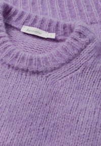 Lila neulepaita, jossa on resoritekstuuri, pyöreä kaula-aukko ja pehmeä, pörröinen materiaali. Varustettu pienellä kangastunnuksella, jossa on brändin nimi ja koko.