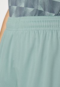 Shorts de sport en bleu sarcelle clair avec une texture douce et une taille élastique. Présente un tissu à motifs géométriques en haut.