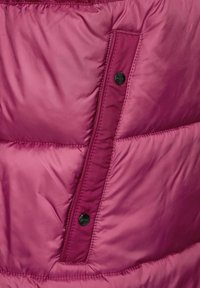 Fuchsia dunjakke-sektion med synlige sømdetaljer, en sidelomme sikret med en sort trykknap og en glat, skinnende overflade.