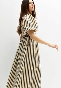 Vestido maxi a rayas con un corsé ajustado, mangas abullonadas y una falda fluida. Los colores son crema y negro, con rayas verticales.