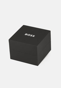 Caja cuadrada negra hecha de papel suave con un logo plateado de "BOSS" en la parte superior. La caja tiene una tapa removible y un diseño limpio y minimalista.