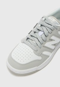 Ljusgrå sneakers med en slät skinnöverdel, perforerad tån, texturerade snören och en vit gummisula med mönstrade accenter.