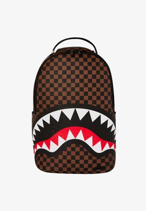Mochila a cuadros marrón y negro con un gran diseño estilizado de boca de tiburón que presenta dientes blancos y lengua roja. Superficie texturizada.