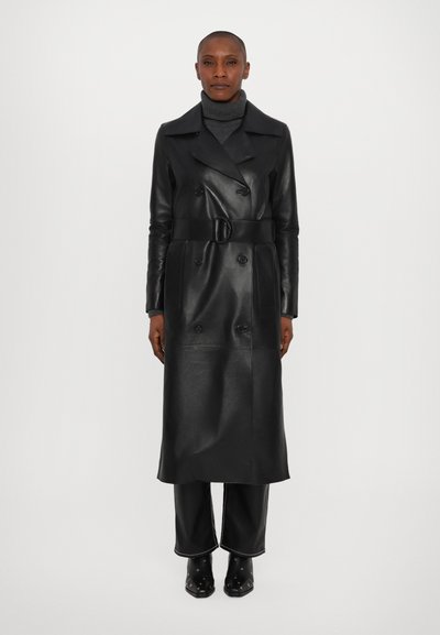 Sort læder trench coat med dobbeltstående design, brede revers, bælte i taljen og lange ærmer. Glat tekstur med fremtrædende knapper.