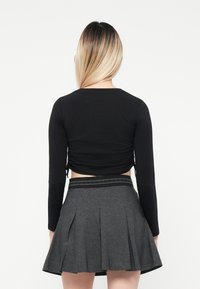 Black long-sleeve cropped top with side ties, paired with a gray pleated skirt featuring a black patterned waistband.
