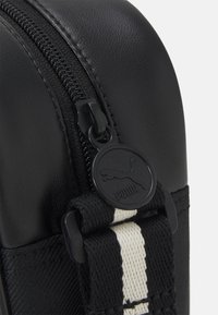 Schwarze, mit Reißverschluss versehene Tasche mit einer glatten, synthetischen Textur. Verfügt über ein auffälliges, schwarzes Puma-Logoschild und ein strapazierfähiges gestreiftes Riemen-Detail.
