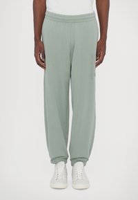 Svijetlozelene trenirke s elastičnim pojasom, sužavaju se na gležnjevima i imaju bočne džepove. Jednostavan dizajn s diskretnim logotipom na bedru.