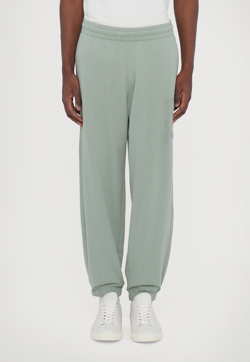 Svijetlozelene trenirke s elastičnim pojasom, sužavaju se na gležnjevima i imaju bočne džepove. Jednostavan dizajn s diskretnim logotipom na bedru.