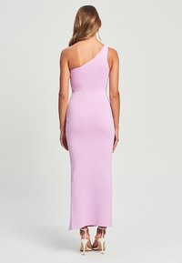 Robe asymétrique rose à une épaule, design ajusté, tissu extensible doux, longueur mi-mollet, style minimaliste, associée à des talons de couleur claire.