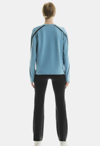 Haut à manches longues bleu clair avec des accents noirs, associé à un pantalon noir, présenté de dos avec une coupe décontractée et une texture douce.