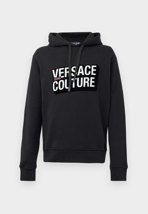 Fekete kapucnis pulóver pamutból, kiemelkedő fehér logóval, amelyen nagybetűkkel az áll: "VERSACE JEANS COUTURE".