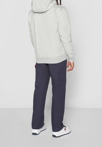 Sudadera gris con capucha, combinada con pantalones cargo azul marino con bolsillos laterales, complementada con zapatillas blancas con detalles en azul.