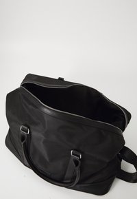 Black travel bag made of durable fabric, featuring a zip closure, dual top handles, and a spacious interior without visible pockets.