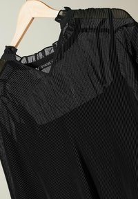 Schwarzes plissiertes Oberteil mit V-Ausschnitt, aus transparentem Stoff gefertigt. Es hat eine strukturierte Oberfläche und einen glatten Halsauschnitt mit dezenten Details.