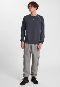 Langärmliges, dunkelgraues Hemd mit kontrastierenden, hellgrauen Nähten, kombiniert mit hellgrauen Cargo-Hosen mit Seitentaschen und elastischen Bündchen.