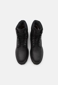 Bottes en cuir noir avec bout arrondi, col rembourré et œillets en métal pour les lacets. Présente une doublure intérieure texturée et une semelle en caoutchouc robuste.