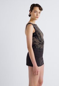 Zwarte tie-dye mouwloze top gecombineerd met high-waisted, zwarte shorts. De stof lijkt glad, met een lichte glans en subtiele textuur.