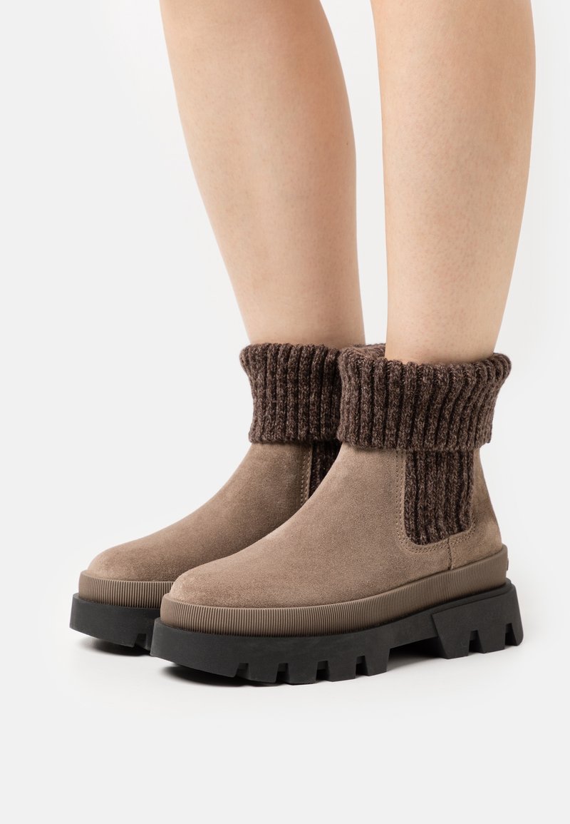Brązowe zamszowe botki za kostkę z prążkowanym ciemno-brązowym ścianką i czarną grubą podeszwą. Gładka tekstura i prosty design.