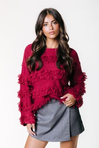 Pull en tricot bordeaux avec des motifs horizontaux froncés, doté de manches longues. Assorti à une mini-jupe grise à rayures.