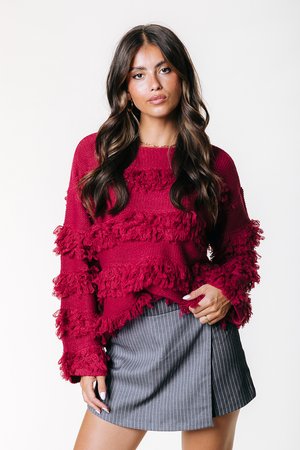 Pull en tricot bordeaux avec des motifs horizontaux froncés, doté de manches longues. Assorti à une mini-jupe grise à rayures.