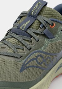 Chaussures de course Saucony Peregrine 15 en olive avec dessus en mesh, lacets bleus et accents orange. Présente des détails texturés et un logo.