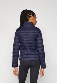 Veste à col montant en duvet marine, avec un design matelassé et des manches longues. Le tissu est lisse avec un léger éclat. Conçue pour une silhouette ajustée.
