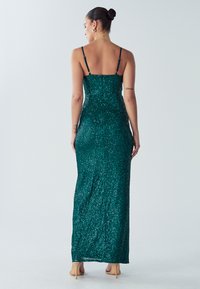 Smaragdgrøn, palietbelagt midi-kjole med spaghetti-stropper, figursyet silhuet og en glat, tekstureret finish; slidse detaljer bagpå.