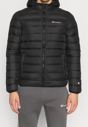 Chaqueta de abrigo negra con capucha, con acolchado horizontal, cierre de cremallera, bolsillos laterales y un pequeño logo blanco en el pecho y la manga.
