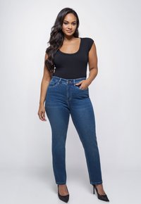 Zwarte scoop-neck bodysuit, hoog getailleerde blauwe jeans en zwarte puntige hakken. Gladde stof, contrasterende texturen, aansluitende silhouet.