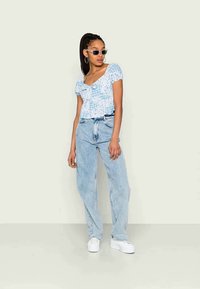 Blusa curta floral azul clara com mangas curtas, combinada com jeans de ganga claros de cintura alta e ténis brancos de plataforma.